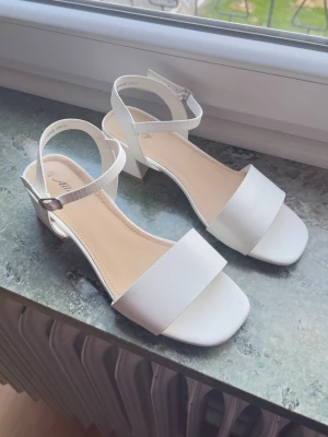 Vita klackskor/sandaler – storlek 40 - Eleganta vita sandaler med låg klack och justerbart ankelband. Perfekta till student, bröllop, fest eller sommarens finare tillfällen. Bekväma att gå i och stilren design som passar till mycket.  Storlek: 40 Färg: vit Skick: fint begagnat skick med mindre spår av användning.  Hör av dig vid frågor eller intresse!