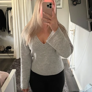 Grå stickad tröja med v-ringning - Säljer en mysig grå stickad tröja med v-ringning och långa ärmar. Perfekt för kyligare dagar. Tröjan har en bekväm passform och ribbade muddar vid ärmslut och nederkant💗