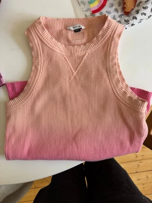 Rosa ribbad linnetopp från H&M - Snygg ribbad linnetopp från H&M i en ombre färgskala från ljusrosa upptill till mörkare rosa nedtill. Ärmlös modell med rund halsringning och stretchigt material. Perfekt för varma dagar eller lager på lager.