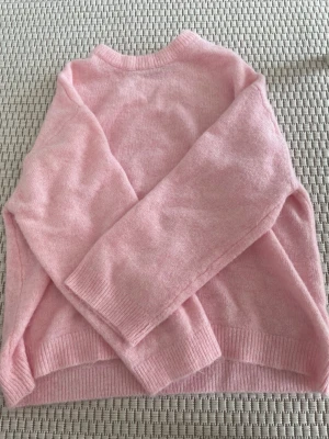Ljusrosa stickad tröja i S - Mysig ljusrosa stickad tröja med rund hals och långa ärmar. Tröjan har ribbade muddar vid ärmslut och nederkant, perfekt för att hålla värmen. Enkel och stilren design som passar till många olika outfits.