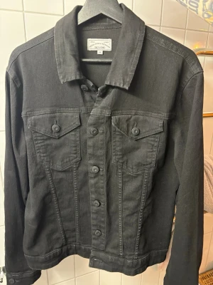 Svart jeansjacka från Only & Sons - Snygg svart jeansjacka från Only & Sons i klassisk modell med knäppning framtill och två bröstfickor med lock. Jackan har raka linjer, krage och långa ärmar. Perfekt för en cool och avslappnad stil.