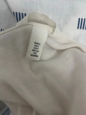 Vit ribbad kofta  - Säljer en vit ribbad kofta från H&M med v-ringning och knappar framtill. Koftan har lång ärm och sitter figurnära, perfekt att styla med jeans eller kjol. Enkel och stilren design som passar till många olika looks.