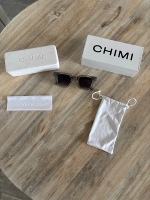 Grå CHIMI 04 solglasögon med tillbehör - Snygga solglasögon från CHIMI i transparent grått acetat med mörka fyrkantiga glas. Kommer med originalfodral, putsduk, förvaringspåse och box. Perfekt accessoar för att lyfta din stil och skydda ögonen mot solen. Andvänt sparsamt. Pris går självklart att diskutera.