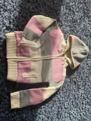 Randig teddyjacka med huva från Sublevel - Mysig teddyjacka från Sublevel med breda ränder i rosa, grått och vitt. Jackan har dragkedja, två fickor fram och en stor huva med dragsko. Insidan är fodrad med fluffigt teddyfoder för extra värme. Perfekt för kalla dagar och riktigt skön att bära.