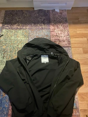 Svart vindjacka från Jack & Jones - Snygg svart vindjacka från Jack & Jones med huva och dragkedja framtill. Jackan har två fickor med dragkedja och meshfoder på insidan för extra komfort. Perfekt för blåsiga dagar och enkel att matcha med olika outfits.