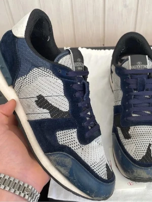 Valentino rockrunners - Snygga sneakers från Valentino med ovandel i blå mocka och grå mesh, detaljer i svart och vitt samt klassisk logga på plösen. Skorna har lågt skaft, vita sulor och mörkblå snören. Perfekta för dig som gillar exklusiva och trendiga sneakers.