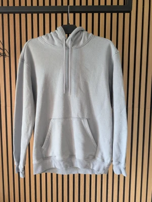 Ljusgrå hoodie med magficka - En stilren ljusgrå hoodie med huva och dragsnören. Hoodien har en klassisk magficka och ribbade muddar vid ärmslut och nederkant. Perfekt för en avslappnad och trendig look. Materialet känns mjukt och bekvämt mot huden.