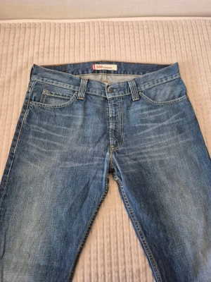 Vintage Levi's 506 jeans - Klassiska blå vintage jeans från Levi's modell 506 Standard med rak passform och fem fickor. Jeansen har snygga slitningar och kontrastsömmar. Tillverkade i slitstark denim, perfekt för en avslappnad och cool stil.