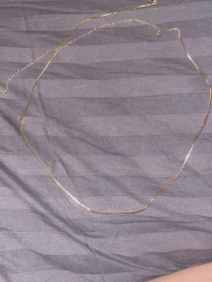 Tunt guld magarmband i minimalistisk stil - Säljer ett supertunt och stilrent halsband i guldfärg. Kedjan är enkel och diskret, perfekt för dig som gillar minimalistiska smycken. Passar snyggt både till lager-på-lager eller som ett subtilt statement.