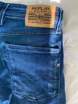 Blå jeans från Replay W33 L32 - Snygga blå jeans från Replay med klassisk femficksdesign och läderpatch bak i midjan. Jeansen har en något tvättad look och är tillverkade i stretchig denim för extra komfort. Perfekta för en trendig och avslappnad stil. Nypris 1500 mitt pris 300. Sparsamt använda.  