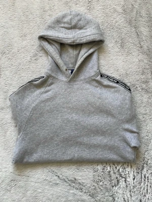 Grå hoodie med textdetaljer - Snygg grå hoodie med huva och svart-vita textdetaljer längs axlarna där det står 'Los Angeles”! Den är använt tidigare men funkar! Priset kan diskuteras.