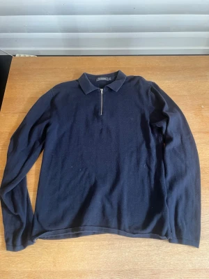 Mörkblå långärmad tröja med dragkedja - Snygg mörkblå långärmad tröja från Oscar Jacobson med krage och kort dragkedja framtill. Tröjan har en klassisk och stilren design, perfekt för en clean look. Materialet känns mjukt och bekvämt mot huden.