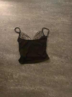 Spiky push up linne  - Snygg svart topp med smala axelband och  silverfärgade spikar nitar på bystdelen. Toppen har en figurnära passform och är perfekt för att skapa en cool och trendig look.