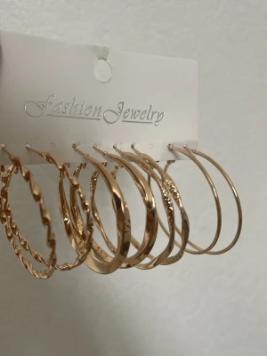 Set med guldiga hoops örhängen - Säljer ett set med sex par guldiga hoops örhängen i olika storlekar och mönster. Några är släta, andra har tvistad eller hamrad yta. Perfekta för att mixa och matcha till olika outfits. Materialet är metall med guldfinish.