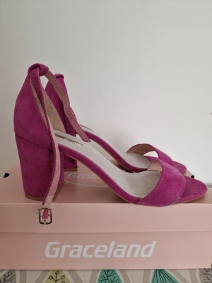 Rosa pumps med blockklack från Metro - Snygga rosa pumps från Metro med öppen tå och bred blockklack. Skorna har en rem runt vristen med spänne och är tillverkade i mockaimitation. Perfekta för dig som vill sticka ut med färg och stil. Köpt utomlands. Storlek 40. Använda en gång. 