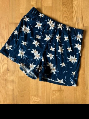 Blommiga blå shorts med resårmidja s/m - Mörkblå shorts med vitt blommönster och elastisk midja. Perfekta för varma dagar och har en avslappnad passform. Tillverkade i mjukt material som känns skönt mot huden.
