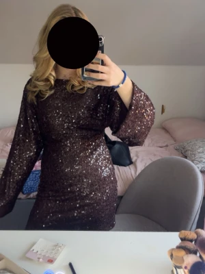 Brun paljettklänning med vida ärmar - Säljer en brun kortklänning täckt av glittriga paljetter. Klänningen har vida långärmar och en rund halsringning. Bara använd en gång! Ny pris är 599. 