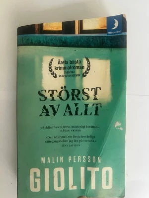 Störst av allt av Malin Persson Giolito - Ene spännande kriminalroman i pocketformat, 'Störst av allt' av Malin Persson Giolito. Omslaget är grönt med svart och vit text. Boken handlar om en rättegång och skildrar en dramatisk tragedi i överklassen. Perfekt för dig som gillar deckare och spänning.