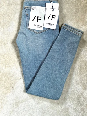 Blå skinny jeans från Selected Femme - Snygga blå skinny fit jeans från Selected Femme. Klassisk femficksmodell med hög midja och smal passform hela vägen ner. Tillverkade i mjukt denimtyg som ger en bekväm känsla och stilren look. Perfekta för dig som gillar en tidlös och enkel stil.