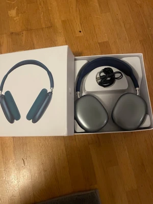 Blå Apple AirPods Max hörlurar - Snygga over-ear hörlurar från Apple i blått med stilren design och mjuka öronkuddar. Tillverkade i aluminium och rostfritt stål med ett vadderat huvudband för extra komfort. Levereras i originalförpackning med laddkabel.