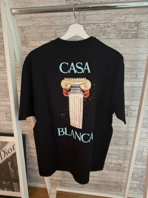 Svart Casa Blanca t-shirt med tryck Xl storlek - Svart t-shirt från Casa Blanca med stort grafiskt tryck av en klassisk pelare och texten 'Casa Blanca' på både fram- och baksidan. T-shirten har rund hals och korta ärmar. Tillverkad i mjuk bomull för en bekväm känsla.