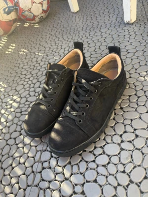 Svarta sneakers med röd sula - Snygga svarta sneakers i mocka med svarta skosnören och cool röd sula. Insidan är beige och skon har en klassisk låg profil med rund tå och dragflik bak. Perfekta för dig som vill ha en stilren men ändå unik look.
