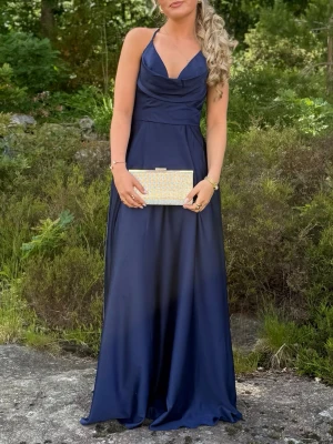 Marinblå långklänning med smala band - Elegant marinblå långklänning med smala axelband och djup v-ringning. Klänningen har en mjukt draperad överdel och faller snyggt i ett glansigt material, perfekt för bal eller fest. Stilren och tidlös design som ger en lyxig känsla. Stl M men sitter som en S 