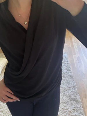 Svart omlottopp med lång ärm - Snygg svart omlottopp med lång ärm och draperad front. Toppen har en v-ringad skärning och sitter figurnära. Perfekt att styla med både jeans och kjol för en trendig look. Från dyra märket inwear