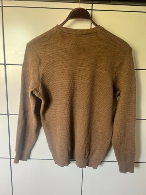 Brun stickad tröja med rund hals - En enkel och stilren brun stickad tröja med rund halsringning och långa ärmar. Tröjan har en ribbad kant vid hals, ärmslut och nederkant. Perfekt för lager på lager under kyliga dagar. Obs storlek som en medium M