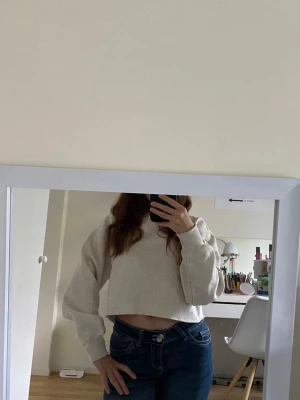 Beige croppad sweatshirt - Säljer en vit croppad sweatshirt med rund hals och långa ärmar. Tröjan har en enkel och stilren design utan tryck eller mönster, och är gjord i mjukt sweatshirtmaterial. Perfekt för en avslappnad och trendig look.