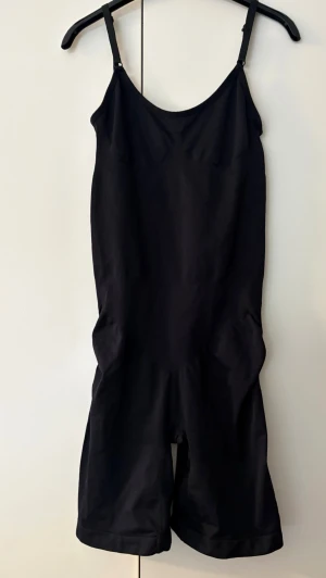 Svart shapewear bodysuit strl.XL - Säljer en svart shapewear bodysuit med justerbara smala axelband och ben som går till mitten av låret. Materialet är stretchigt och formar kroppen snyggt. Perfekt under tighta kläder för en slät siluett. Storlek XL. Öppning i grenen.