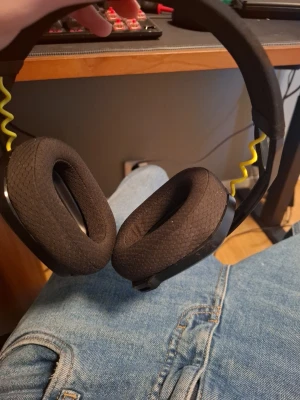 Svarta over-ear hörlurar med gul detalj - Snygga svarta over-ear hörlurar med mjuka, vadderade öronkuddar i tyg och en cool gul spiralformad kabel på båda sidor. Bågen är klädd i tyg för extra komfort och designen är modern och stilren. Perfekta för gaming eller musiklyssning.