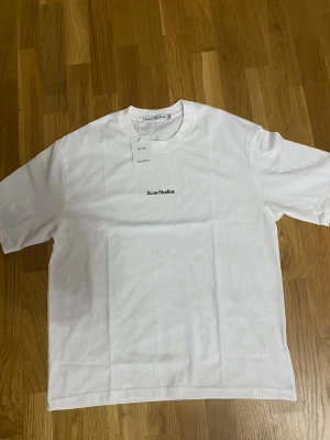 Vit t-shirt från Acne Studios - Klassisk vit t-shirt från Acne Studios med diskret logga tryckt på bröstet. T-shirten har rund halsringning och korta ärmar. Tillverkad i mjuk bomull för en clean och stilren look.