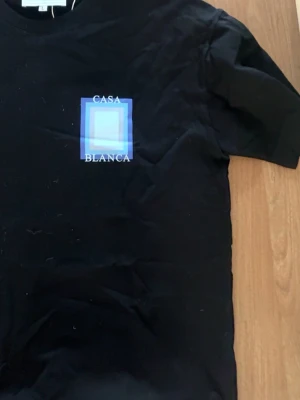 Svart t-shirt från Casablanca - Snygg svart t-shirt från Casablanca med tryck i blått och vitt på bröstet där det står 'Casa Blanca'. Klassisk passform och rund hals. Tillverkad i mjuk bomull som känns skön mot huden. Perfekt för dig som gillar stilrena plagg med en twist. Finns i M och L!🙃 kan gå ner i pris vid snabb affär 