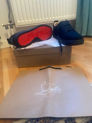 Svarta sneakers från Christian Louboutin - Stilrena svarta sneakers från Christian Louboutin med klassisk röd sula och svarta skosnören. Ovandelen är i mocka och insidan är ljus. Perfekta för dig som vill ha en lyxig och ikonisk sneaker med snygga detaljer.