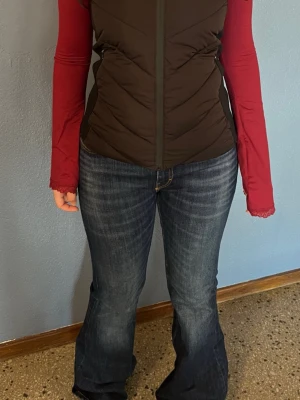 Svart zaraväst - Snygg svart zaraväst med figurnära passform och dragkedja framtill. Västen har en praktisk huva och diskreta sidfickor. Perfekt att slänga över en hoodie eller långärmad tröja för extra värme. Materialet är quiltat och ger en sportig look.
