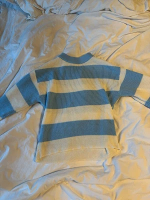 Blåvit randig stickad tröja - Säljer en stickad tröja från Gina Tricot med breda blå och vita ränder. Tröjan har rund halsringning och långa ärmar. Materialet känns mjukt och bekvämt, perfekt för kyligare dagar. 