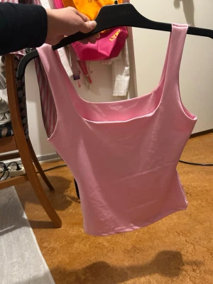 Ljusrosa ärmlös linnetopp - Snygg ljusrosa linnetopp med breda axelband och fyrkantig ringning. Toppen är croppad och har en enkel, stilren design som passar perfekt till jeans eller kjol. Tillverkad i mjukt material för en bekväm känsla.