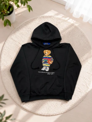 Svart hoodie Polo Ralph Lauren - Svart hoodie från Polo Ralph Lauren med ikoniska Polo Bear-trycket på bröstet. Hoodien har huva med dragsko och en stor magficka. Perfekt för dig som gillar streetwear och klassiska märken.