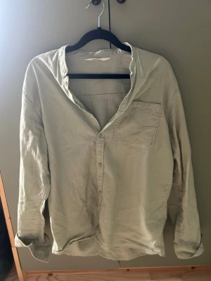 Ljusgrön linneskjorta från H&M - Säljer en ljusgrön skjorta från H&M i mjukt linne. Skjortan har lång ärm, bröstficka och knappar framtill. Perfekt för en avslappnad och stilren look. Passar dig som gillar enkla och svala plagg.