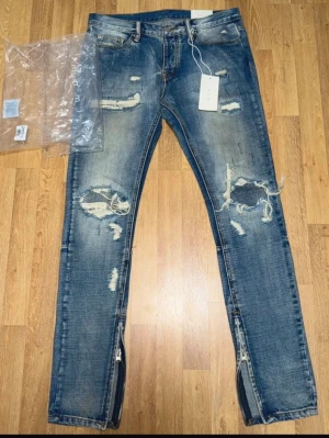 Säljer ett par MNML Repaired Jeans Blue – Size W32 - Jeansen är helt nya och endast testade. Inga skador eller slitage.  Trendiga jeans med ripped/repaired design och dragkedjor vid anklarna som ger en modern streetwear-look. Original tags medföljer.  Size: W32 🏷️ Rabatt vid köp av flera plagg!