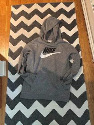 Grå Nike hoodie med logga - Tjena! Säljer min Snygga grå hoodie från Nike med stor svart och vit logga på bröstet. Tillverkad i mjukt material med borstad insida för extra komfort. Klassisk huva och känguruficka framtill. Perfekt för en avslappnad och sportig stil. Passar dig från 158-170 MVH Strwwt Wst 