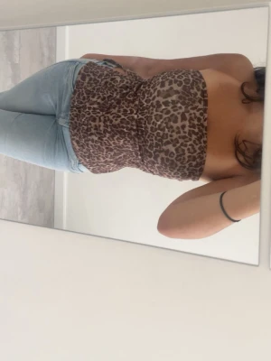 Leopardmönstrad topp  från Pull&Bear - Säljer en leopardmönstrad bandeau topp från Pull&Bear. Toppen är axelbandslös och har en snygg draperad front. Materialet är mjukt och stretchigt, perfekt för att styla med jeans eller kjol. Färgen går i bruna och beige toner.