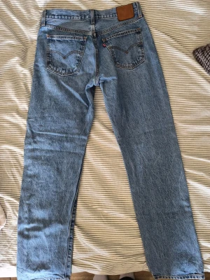 Levi's ljusblå raka jeans - Klassiska ljusblå jeans från Levi's med rak passform och fem fickor. Jeansen har en ikonisk läderpatch bak i midjan och tydliga sömmar. Tillverkade i slitstark denim med vintagekänsla och normal midja. Perfekta för en avslappnad och tidlös stil.