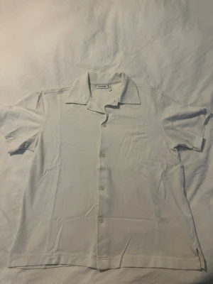 Vit kortärmad skjorta från Weekday - Stilren vit skjorta från Weekday med korta ärmar och klassisk krage. Skjortan har knappar framtill och är tillverkad i mjuk bomull, perfekt för en avslappnad och trendig look. Storlek S men passform som M skulle jag säga. 