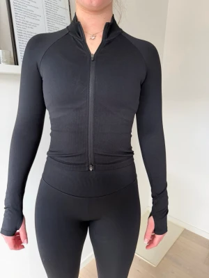 Svart träningströja med dragkedja från amin - Säljer en svart, tight och långärmad träningströja med hel dragkedja framtill. Tröjan har tumhål vid ärmsluten och är tillverkad i ett stretchigt funktionsmaterial som passar perfekt till gymmet eller löpning🔥✨