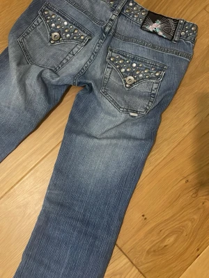 Blå jeans med nitar från BIK BOK - Snygga blå jeans från BIK BOK med silverfärgade nitar på fickorna och linningen. Jeansen har raka ben och dekorativa knappar på bakfickorna. Tillverkade i klassiskt denimtyg med cool tvätt och detaljer som sticker ut.