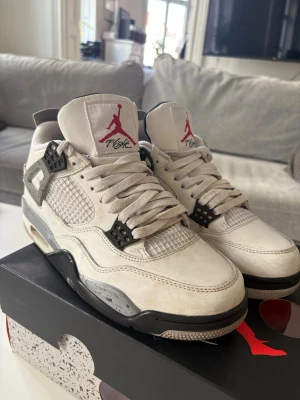Air Jordan 4 White Cement sneakers - Säljer ett par klassiska Air Jordan 4 White Cement sneakers. Skorna är vita med grå och svarta detaljer, meshpaneler och den ikoniska Jumpman-loggan på plösen. Sulan har stänk av grått och svart, och baksidan pryds av Nike Air-loggan. Perfekta för dig som gillar streetwear, lite smutsiga.