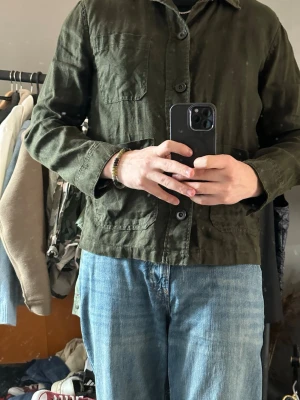 Olivgrön overshirt från h&m  - Stilren olivgrön overshirt från KappAhl Herr, tillverkad i ett mjukt och lätt tyg. Modellen har tre fickor framtill, knäppning med stora knappar och klassisk krage. Perfekt att bära öppen eller stängd över en t-shirt för en avslappnad look.