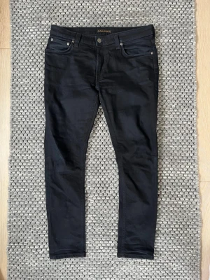 Svarta Nudie Jeans - Säljer nu dessa riktigt snygga Nudie jeans i svart färg🤩💯Storleken är W33 L28 och är mycket bekväma och passar till allt🙌🤩Jeansen är i väldigt bra skick förutom defekten som man ser på bild 2 (byxorna har nån liten fläck) där av priset😁💯Vid frågor och funderingar är det bara att skriva✍️📝
